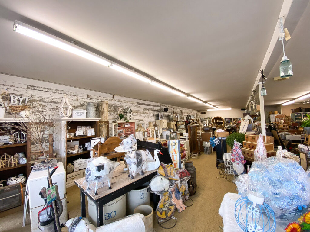 Eclectic antique store aisle with antique furniture, home goods, and plants at Junque Decor Floral and Greenhouse